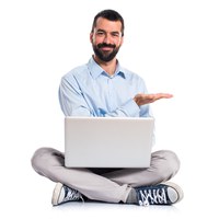 Bearded man sitting cross-legged holding laptop and gesturing to the side